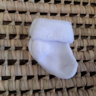 Meia branca para bebé com aba dobrada sobre superfície de palha trançada