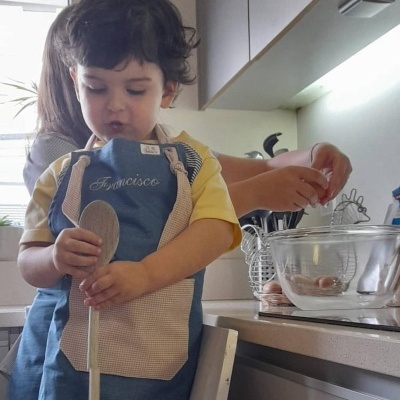 Criança com avental azul a segurar colher de pau numa cozinha moderna