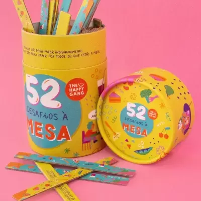 Frasco amarelo com tampa removida e palitos coloridos com padrão colorido, texto 52 DESAFIOS À MESA