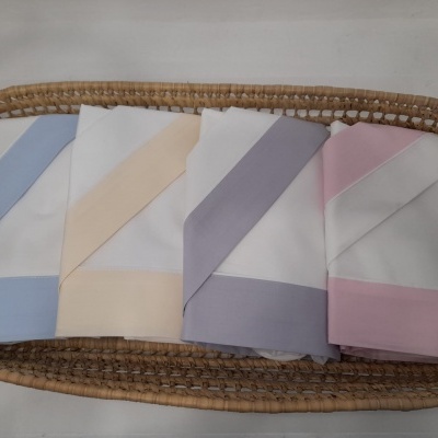 Conjunto de quatro panos brancos com bordas de cores diferentes numa cesta de vime