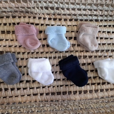 Sete pares de meias de bebé de várias cores sobre superfície de trama natural