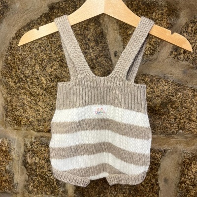 Pieza de roupa de bebé de malha às riscas branco e bege pendurada num cabide de madeira