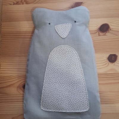 Almofada azul claro com padrão de bolinhas brancas em formato de nariz e barriga sobre madeira clara