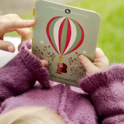 Livro infantil com balão de ar quente na capa, mãos segurando o livro