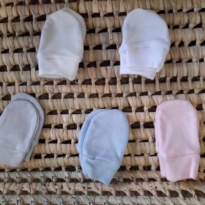 Cinco pares de luvas de bebé em várias cores sobre tecido entrelaçado