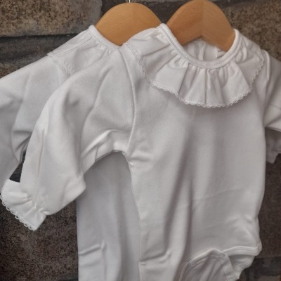 Dois bodies brancos de bebé com gola folhada e punhos rendados pendurados