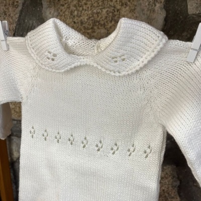 Camisola branca de bebé com gola e padrão de tricô pendurada