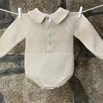 Body de bebé bege claro em malha pendurado num estendal diante de parede de pedra