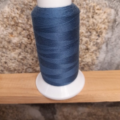 Rolo de linha azul escuro com suporte branco em madeira perante parede de pedra