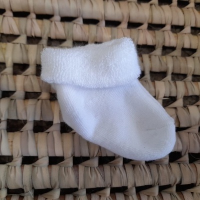 Meia branca pequena em tecido felpudo com bainha dobrada sobre palha entrelaçada