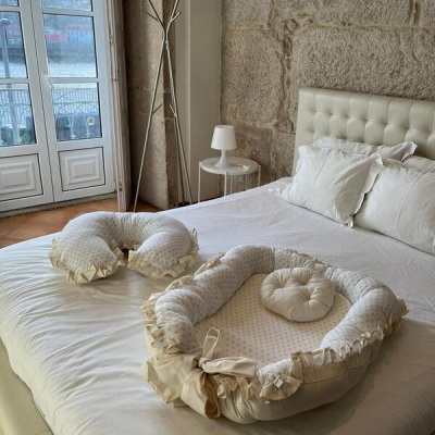 cama branca com almofada em U e ninho de bebé em tecido creme num quarto com parede de pedra