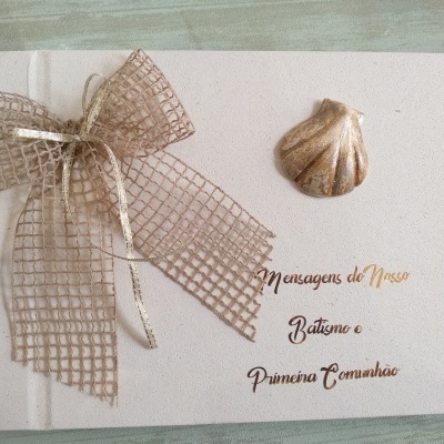 Livro branco com laço em fita castanha e concha, texto sobre Batismo e Primeira Comunhão