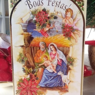 Cartão de Natal com imagem da Sagrada Família, anjos, flores vermelhas e texto Boas Festas