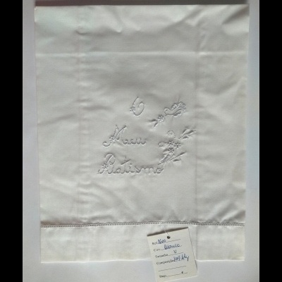Toalha branca com bordado Casa Antunes e etiqueta com descrição do tecido.
