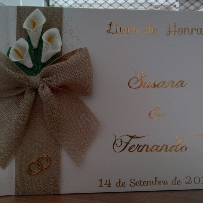 Livro de Honra branco com laço bege e flores brancas, textos dourados e anéis decorativos