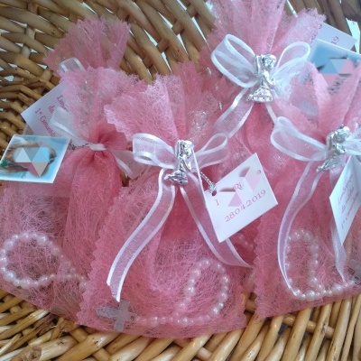 Sacinhos cor-de-rosa com pulseiras de pérolas e laços brancos numa cesta de vime