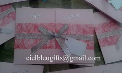 Convite em papel rosa com fitas prateadas e vermelhas e etiqueta branca suspensa