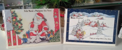 Dois cartões de Natal com imagens de Pai Natal e aldeia nevada com boneco de neve e textos festivos.