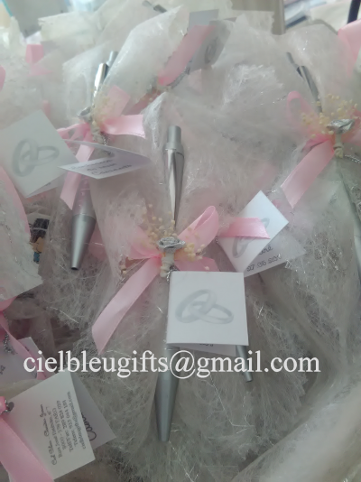 Conjunto de canetas com laços rosa e cartão com alianças, sobre tecido branco