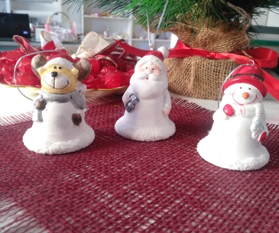 Três figuras decorativas de Natal em cerâmica ou resina sobre tecido vermelho