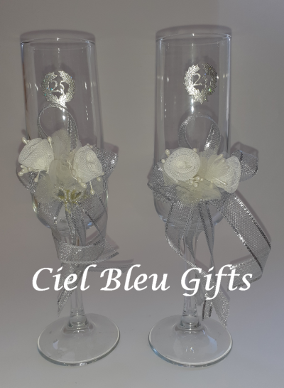 Dois copos de champanhe decorados com flores e laços prateados, em fundo branco