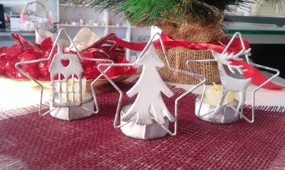 Castiçais metálicos natalícios em forma de casa, árvore e rena sobre mesa com toalha vermelha