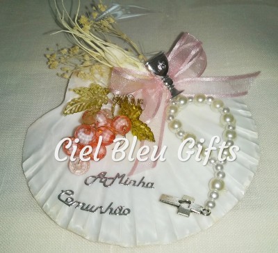 Prato de concha com pulseira de pérolas, flores secas, fita rosa e texto para comunhão.
