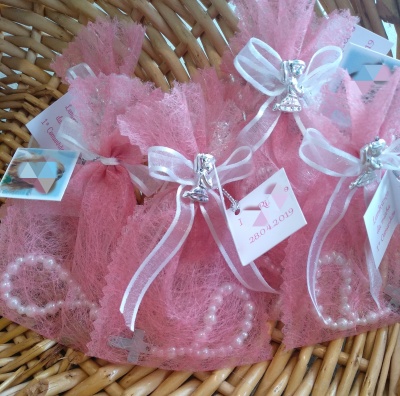 Sacinhos cor-de-rosa com pulseiras de pérolas e laços brancos numa cesta de vime