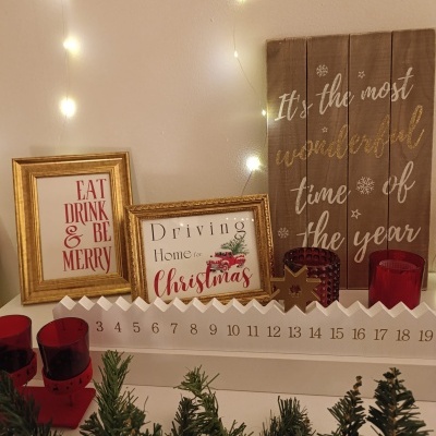 Decoração natalícia com molduras douradas, placa de madeira, velas vermelhas, luzes e calendário de contagem decrescente