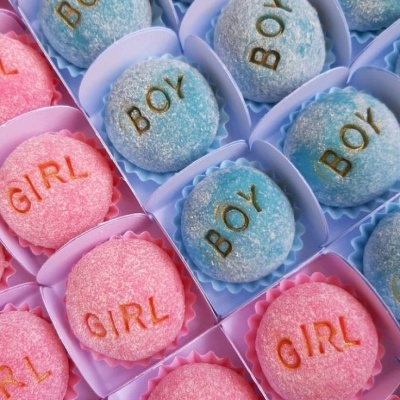 Doces redondos azuis com 'BOY' dourado e rosas com 'GIRL' laranja em caixas individuais