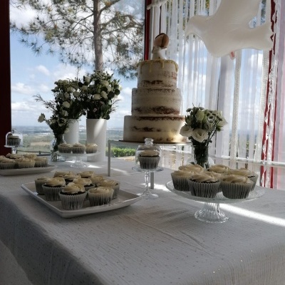 Mesa de bolo e cupcakes decorada para festa com flores e janela ao fundo