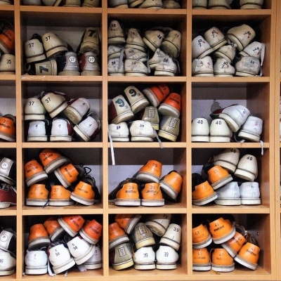 Sapatos de bowling brancos e laranjas organizados em prateleira de madeira por tamanho
