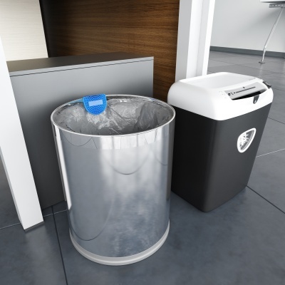 Dois contentores de lixo, um metálico prateado com saco plástico transparente e etiqueta azul, outro de plástico preto e branco com tampa, no chão de azulejos cinzentos.