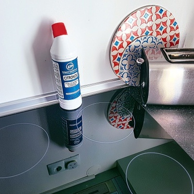 Fogão vitrocerâmico preto com frasco de limpeza CITROMAX e pratos decorativos ao fundo, ao lado uma torradeira metálica.