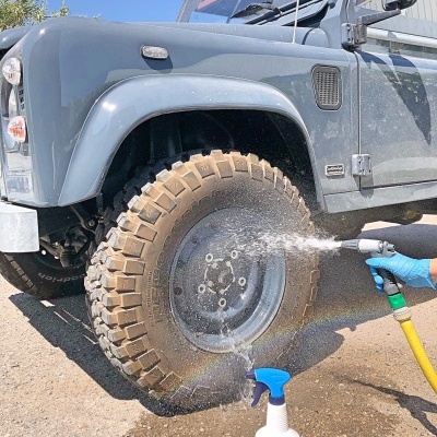 Jipe cinza com pneu a ser lavado com mangueira e frasco de spray na frente.