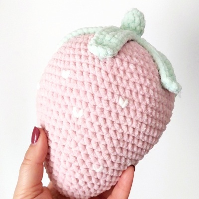 Brinquedo em forma de morango rosa e verde sendo segurado por uma mão