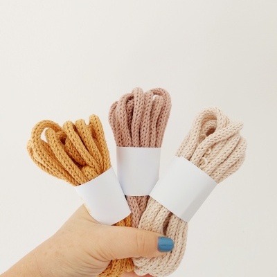 Três cordas grossas enroladas em tons terra, seguradas por uma mão com unha pintada de azul, em fundo branco.