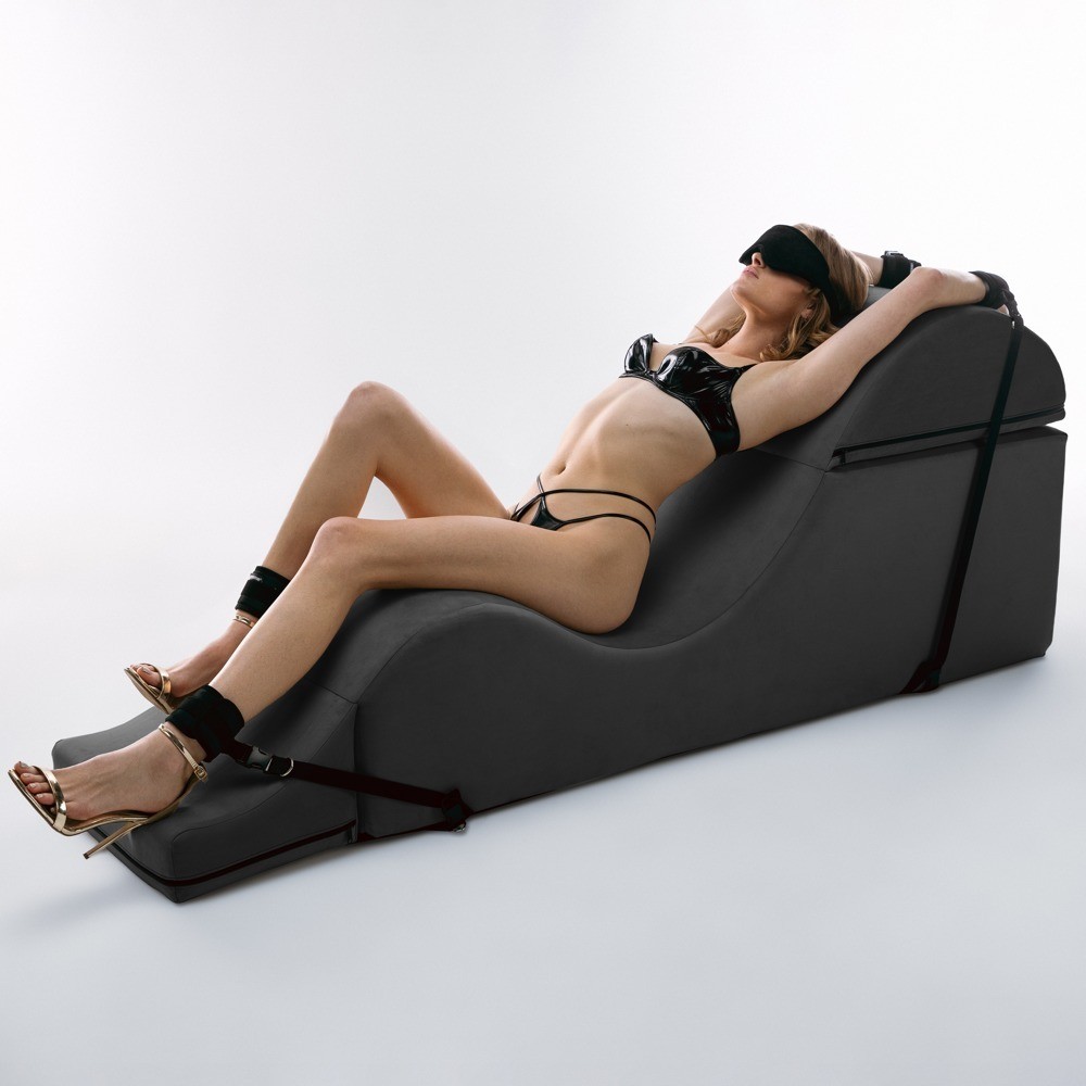 Mulher de lingerie preta e máscara reclinada em cama ergonómica preta com cintas pretas