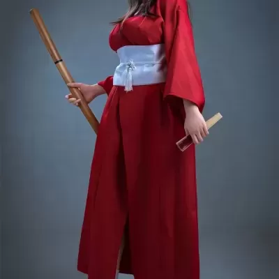 Boneca vestida com quimono vermelho segurando bastão e leque em fundo cinza