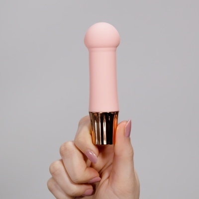 Produto rosa claro com haste dourada segurado por mão feminina com unhas rosas