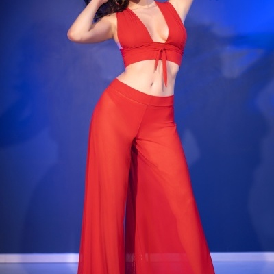 Conjunto feminino vermelho com top decotado, calças largas transparentes e sapatos nude de salto.