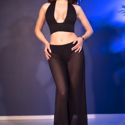 Mulher com top preto cropped e calças transparentes pretas em ambiente interior