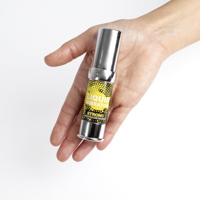 frasco metálico prateado LIQUID VIBRATOR com rótulo amarelo e preto na mão
