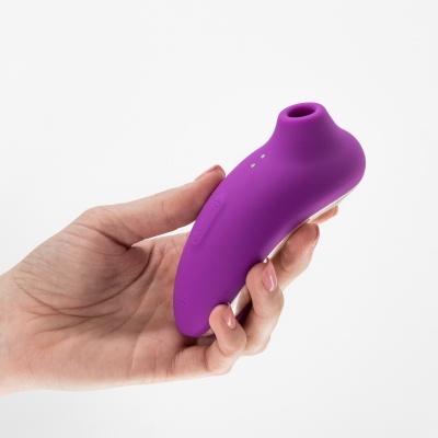 Dispositivo roxo em silicone segurado por mão em fundo branco