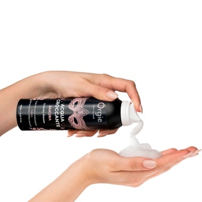 Frasco preto com mousse efervescente branco sendo dispensado em mão, fundo branco