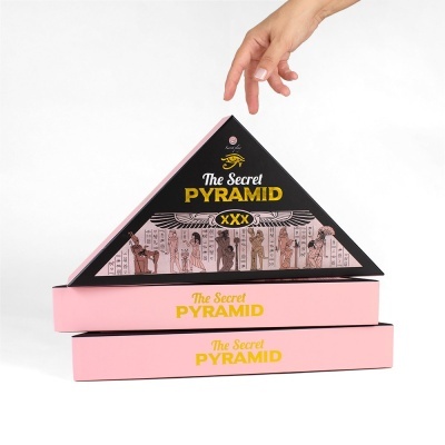 Caixa triangular preta e rosa com texto dourado e branco e ilustrações egípcias, empilhada sobre caixas retangulares rosas