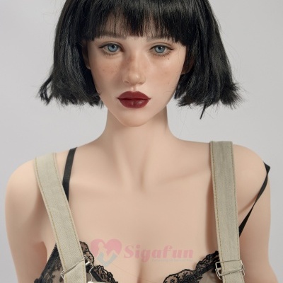 Manequim com cabelo preto e roupa bege e preta, fundo cinzento.