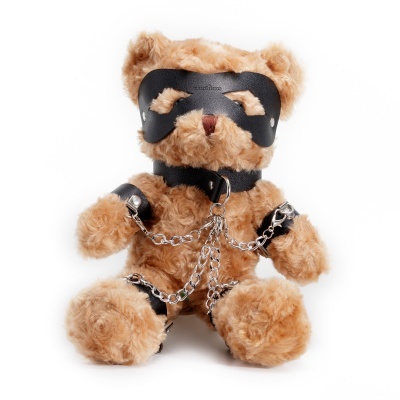Ursinho de peluche castanho com máscara e arnês de couro pretos e correntes metálicas prateadas.