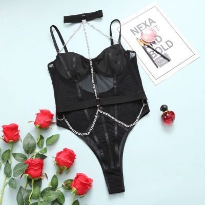 Body lingerie preto com correntes prateadas e tule sobre fundo azul claro com rosas vermelhas e acessórios