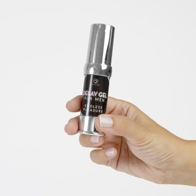 Frasco prateado com rótulo preto e texto DELAY GEL FOR MEN ENDLESS PLEASURE na mão